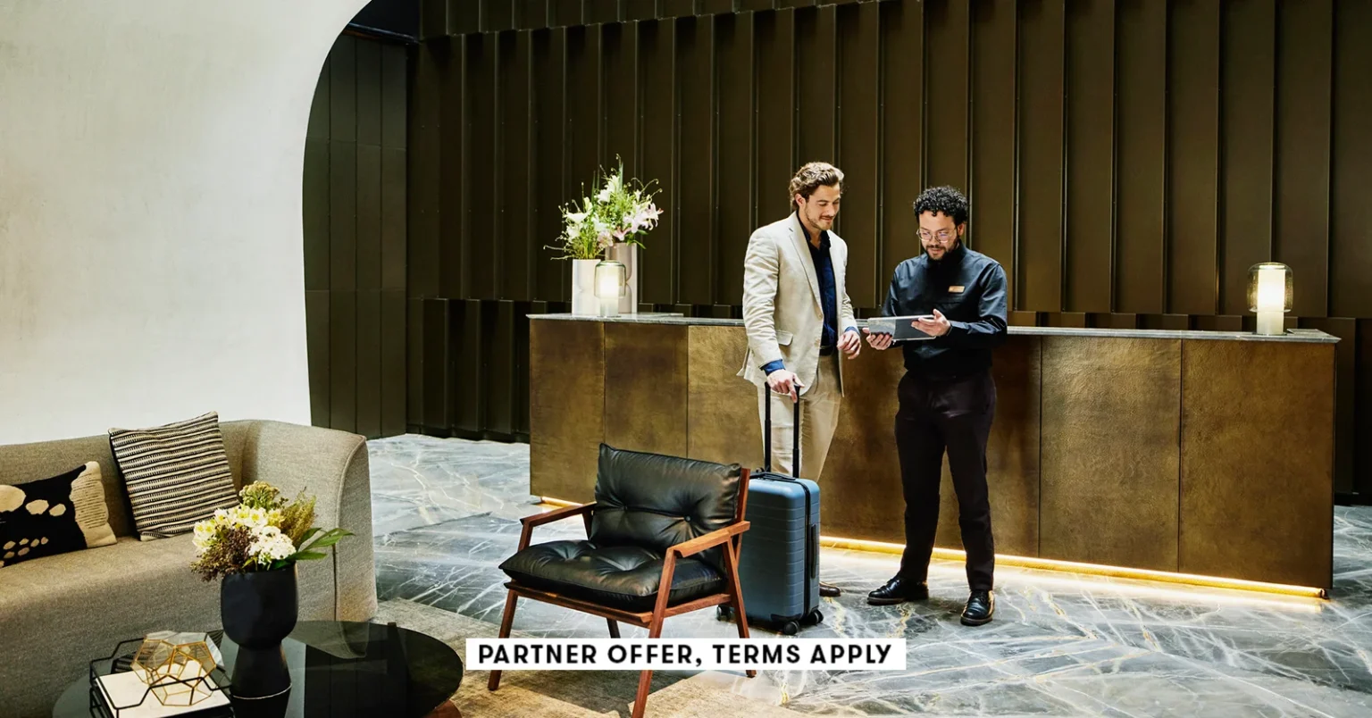 20250715 SOCIAL DISCLAIMER PARTER OFFER TERMS APPLY HOTEL MANAGER CHECKING IN BUSINESSMAN INTO HOTEL.webp