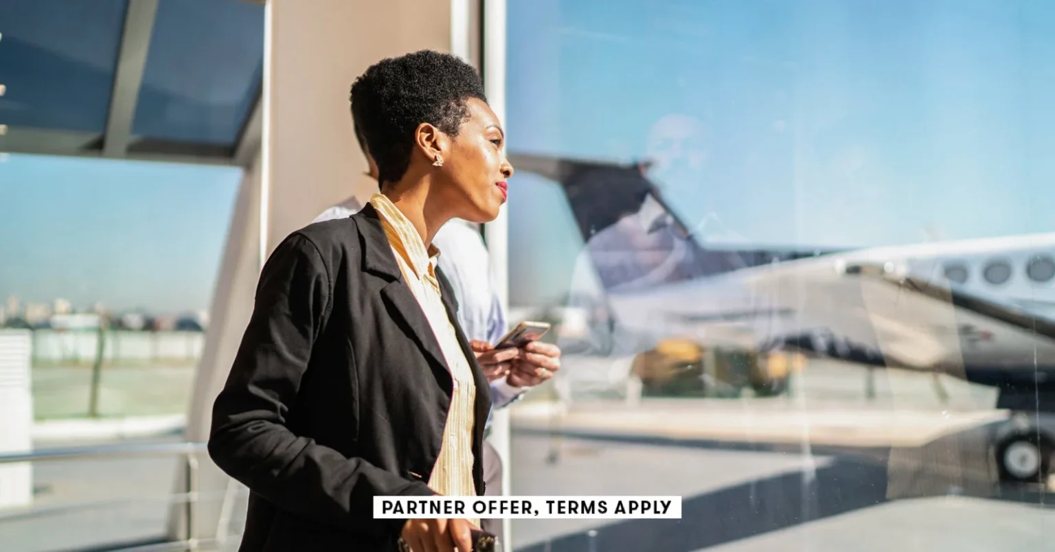 SOCIAL IMAGE PARTNER OFFER TERMS APPLY ooking through the window and using smartphone in the airport.webp